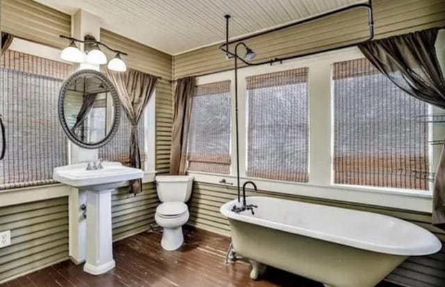 full bath featuring a soaking tub, wood finished floors, and toilet