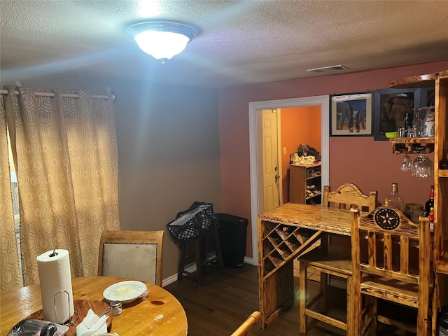 dining space featuring dark wood-type flooring, visible vents, a textured ceiling, and baseboards