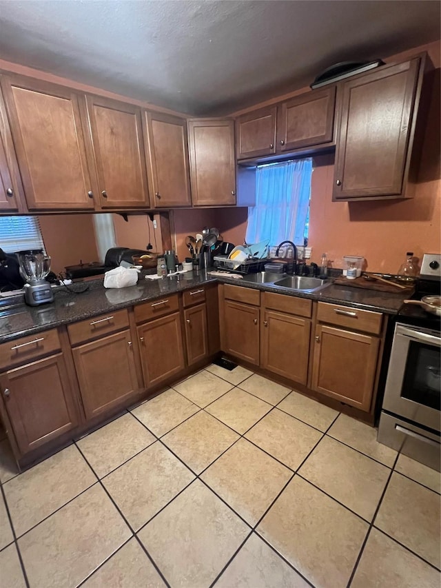 kitchen with stainless steel range with electric stovetop, dark stone counters, a sink, and light tile patterned floors