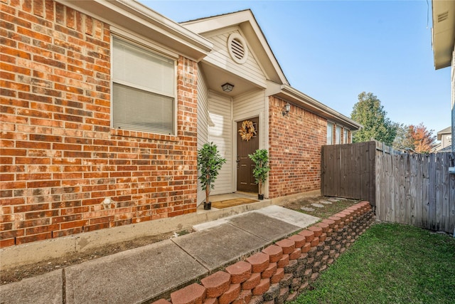 doorway to property featuring brick siding and fence