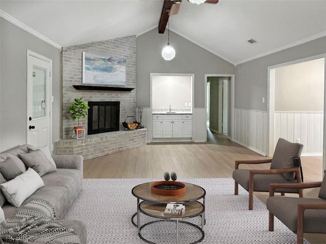 living area with light wood finished floors, visible vents, wainscoting, lofted ceiling with beams, and a fireplace