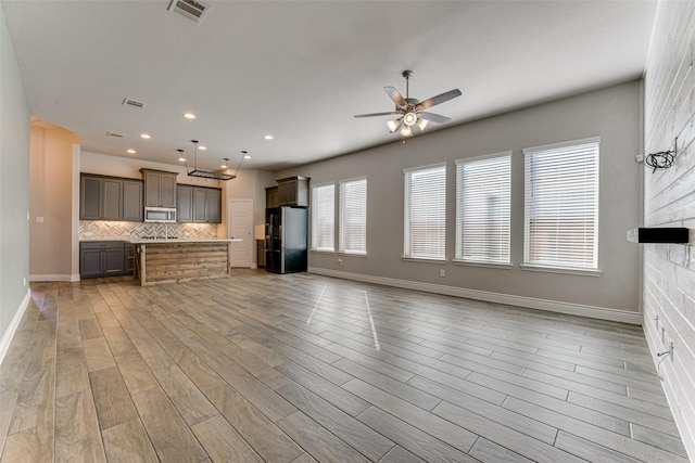 kitchen with stainless steel microwave, hanging light fixtures, gray cabinets, light countertops, and a sink