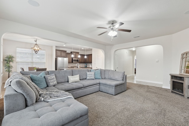 living area featuring visible vents, ceiling fan with notable chandelier, arched walkways, and light colored carpet