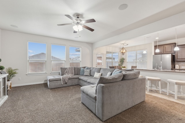 carpeted living area with tile patterned flooring, a healthy amount of sunlight, baseboards, and ceiling fan with notable chandelier