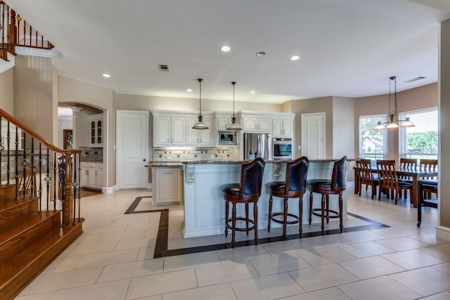 kitchen with stone counters, stainless steel appliances, a spacious island, visible vents, and backsplash