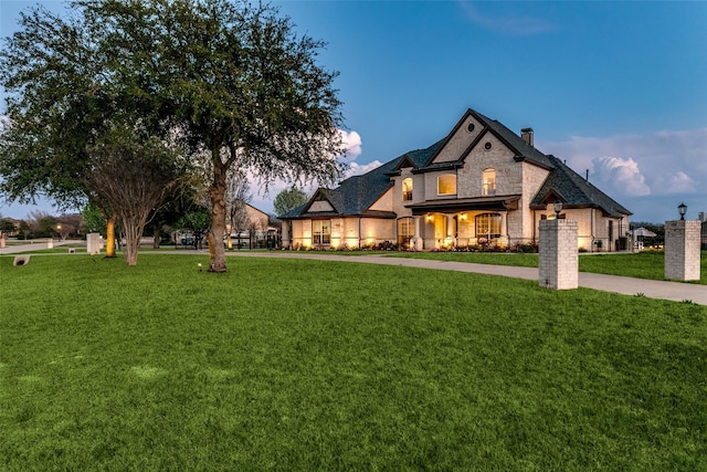 french country inspired facade with driveway, stone siding, and a yard