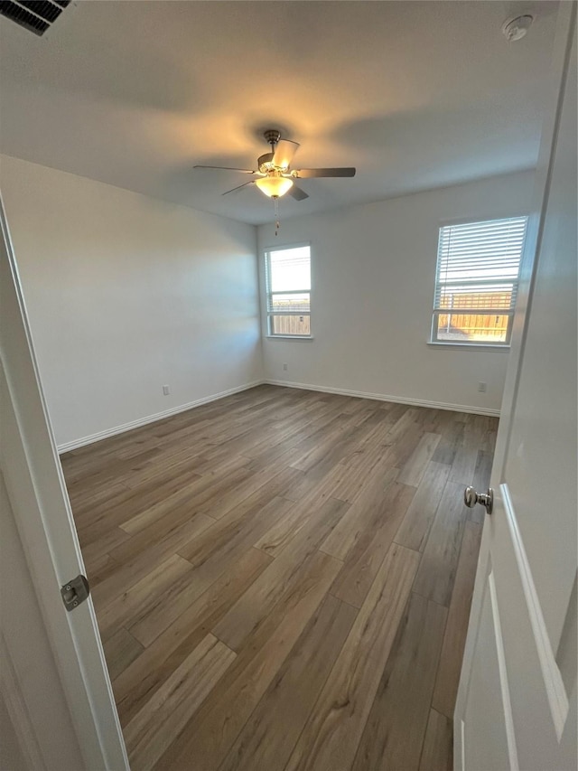 spare room with baseboards, wood finished floors, visible vents, and a ceiling fan