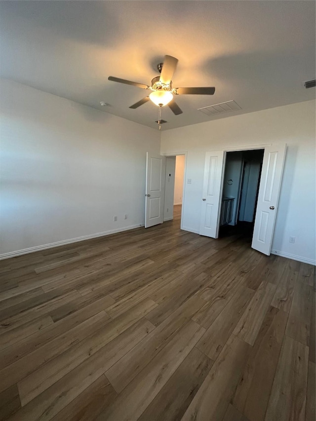 unfurnished bedroom featuring dark wood-style floors, baseboards, visible vents, and a ceiling fan