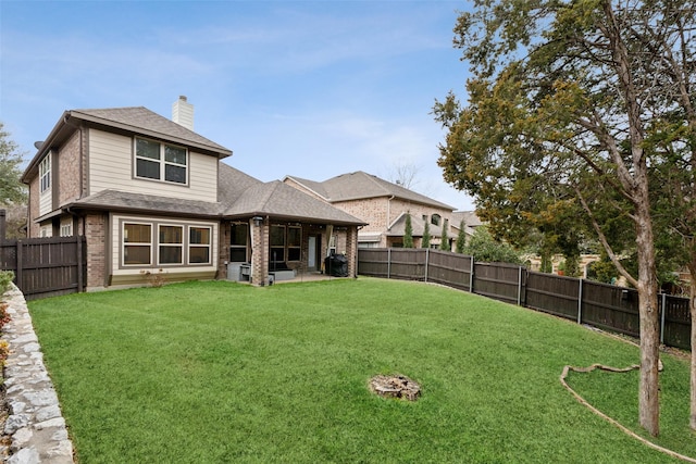 rear view of property with brick siding, a yard, a chimney, roof with shingles, and a fenced backyard