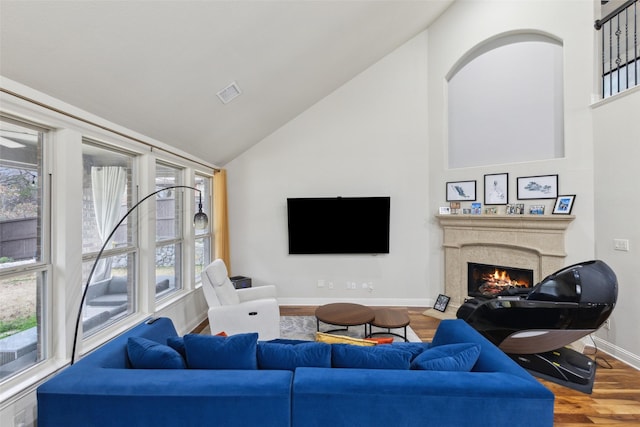 living room featuring visible vents, wood finished floors, high vaulted ceiling, a warm lit fireplace, and baseboards