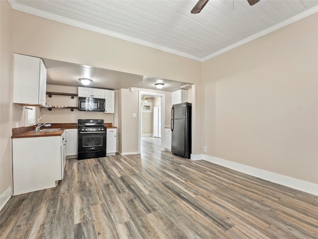 kitchen with a sink, wood counters, white cabinetry, black appliances, and crown molding