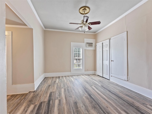 unfurnished bedroom with multiple closets, ornamental molding, an AC wall unit, wood finished floors, and baseboards