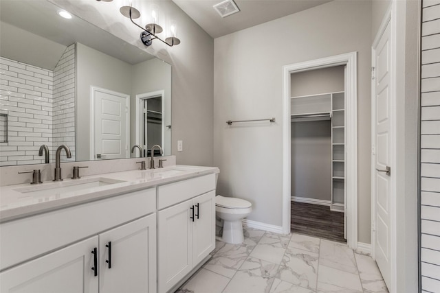 bathroom with marble finish floor, visible vents, a walk in closet, and a sink