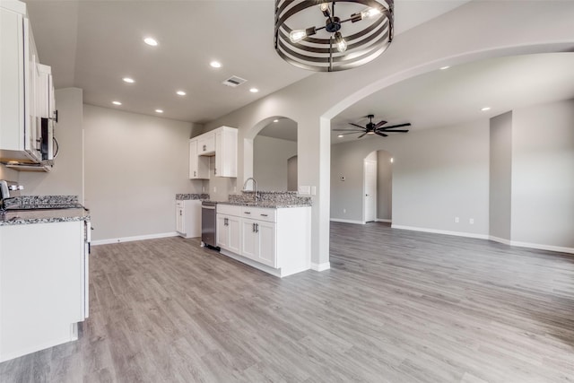 kitchen with ceiling fan, arched walkways, light stone counters, white cabinets, and open floor plan