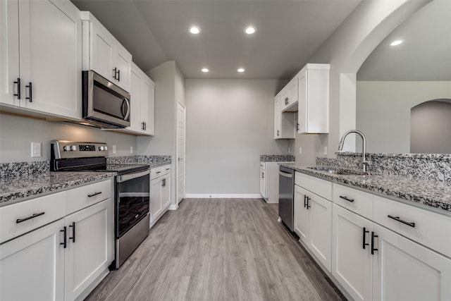 kitchen featuring stainless steel appliances, light stone counters, a sink, and white cabinetry