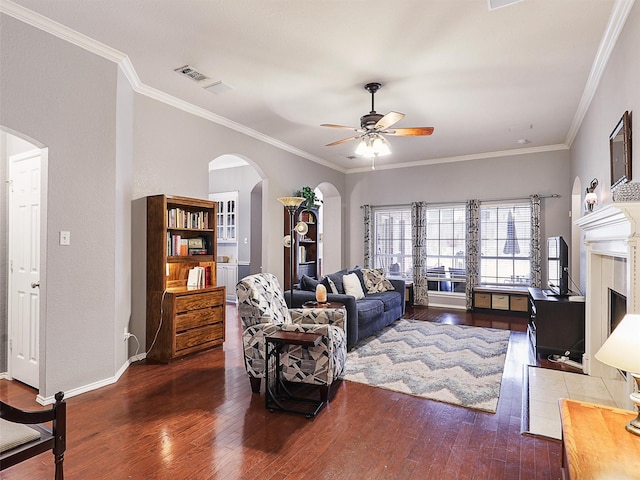 living area featuring arched walkways, a fireplace, a ceiling fan, ornamental molding, and wood-type flooring