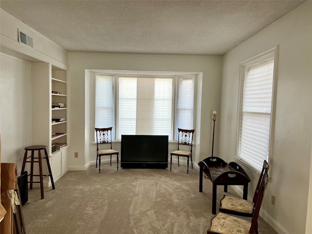 living area with a textured ceiling, carpet floors, visible vents, built in features, and baseboards