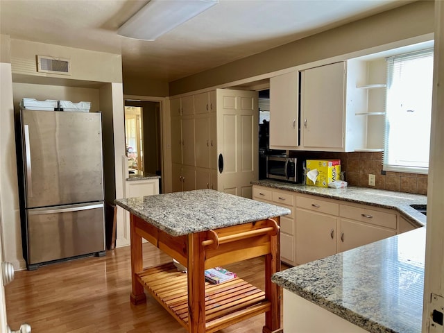 kitchen with visible vents, stainless steel appliances, light wood-type flooring, white cabinetry, and backsplash