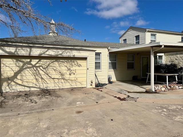 rear view of property featuring an attached garage, a shingled roof, and concrete driveway