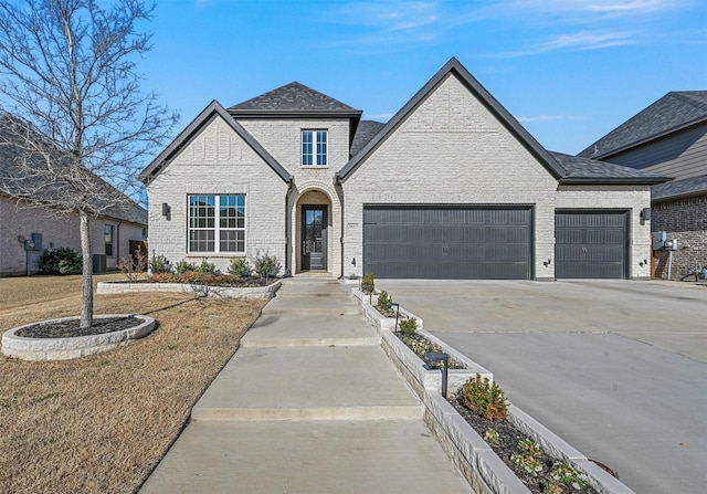 french country inspired facade with a garage, concrete driveway, and brick siding