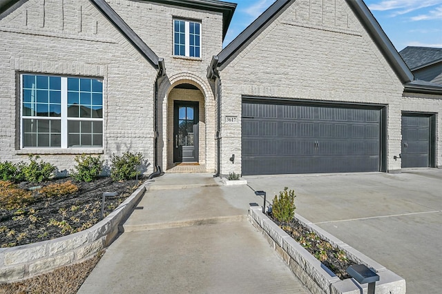 view of exterior entry featuring an attached garage, driveway, and brick siding