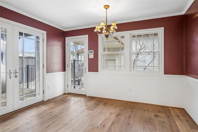 unfurnished dining area featuring french doors, a wainscoted wall, light wood-style flooring, an inviting chandelier, and ornamental molding