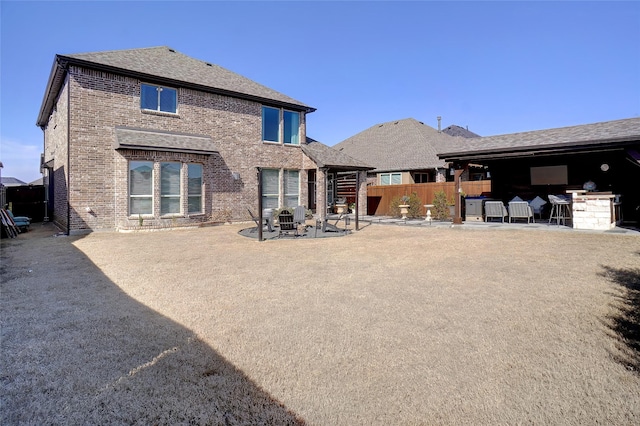 rear view of property featuring roof with shingles, fence, a patio, and brick siding