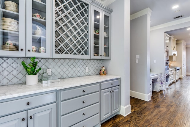 bar with visible vents, backsplash, ornamental molding, dark wood-type flooring, and baseboards