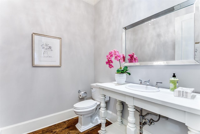 half bathroom with toilet, a sink, baseboards, and wood finished floors