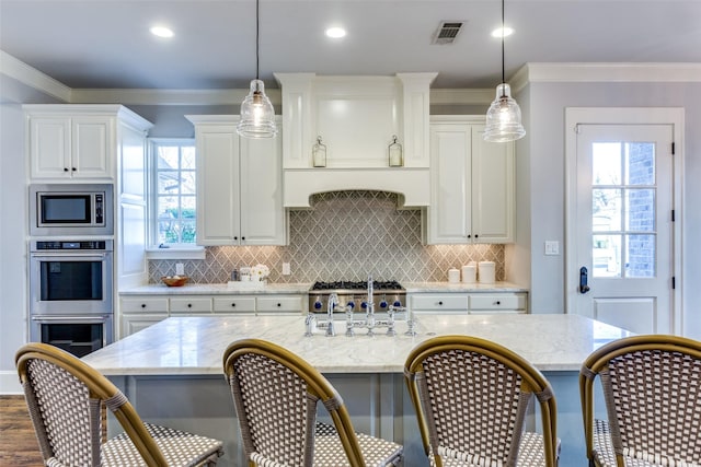 kitchen with a center island with sink, visible vents, light stone counters, decorative light fixtures, and stainless steel appliances