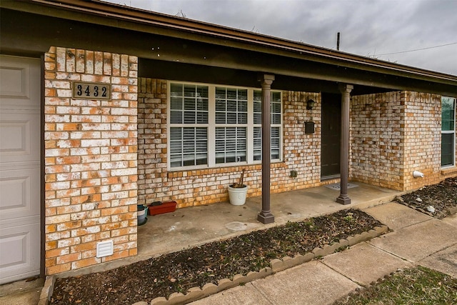 entrance to property featuring a garage, covered porch, and brick siding