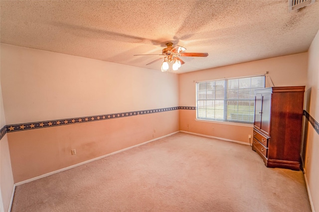 spare room with a textured ceiling, light colored carpet, a ceiling fan, baseboards, and visible vents