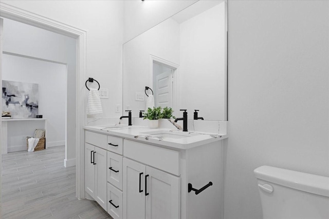 bathroom with wood finished floors, a sink, toilet, and double vanity