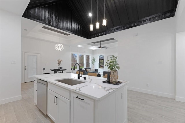 kitchen featuring light stone counters, a sink, white cabinetry, stainless steel dishwasher, and an island with sink