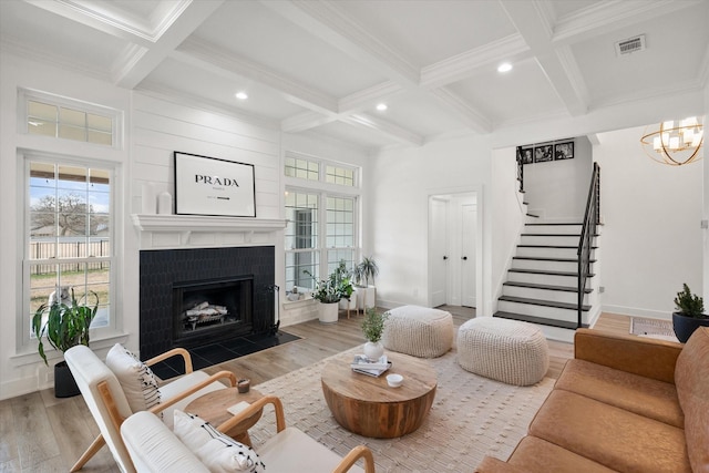 living area with coffered ceiling, a fireplace with flush hearth, visible vents, stairs, and beamed ceiling