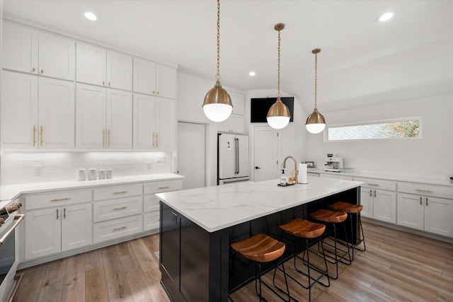 kitchen featuring an island with sink, freestanding refrigerator, and pendant lighting