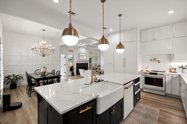 kitchen with an island with sink, a sink, pendant lighting, and high quality stove