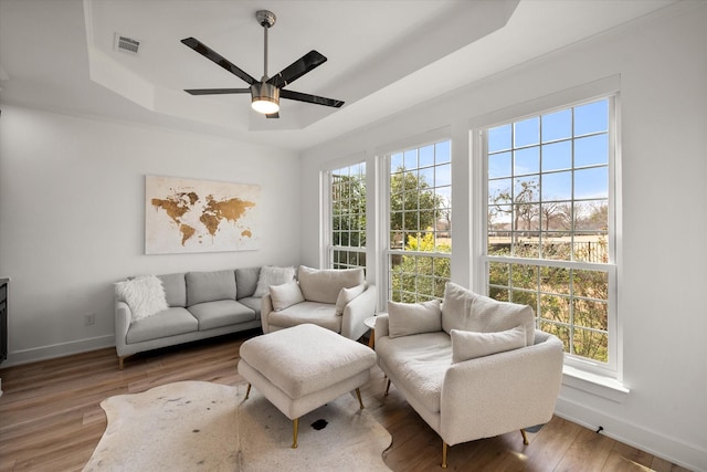 living area featuring a raised ceiling, visible vents, ceiling fan, wood finished floors, and baseboards