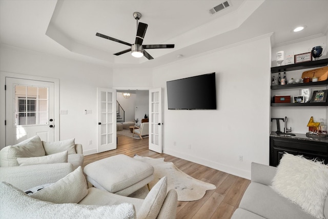 living room featuring visible vents, baseboards, french doors, light wood finished floors, and a raised ceiling