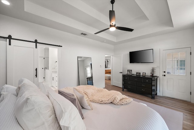 bedroom featuring a barn door, visible vents, a raised ceiling, wood finished floors, and ensuite bathroom