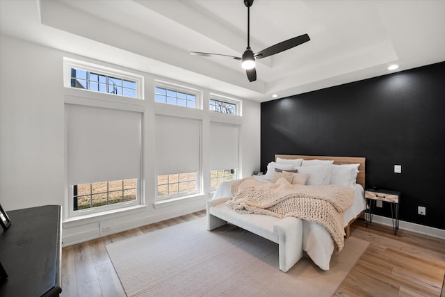 bedroom with an accent wall, light wood-type flooring, a raised ceiling, and baseboards