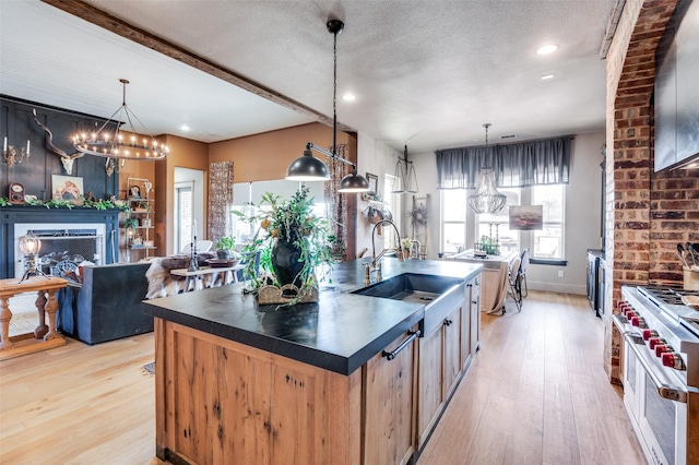 kitchen featuring a center island with sink, range with two ovens, dark countertops, open floor plan, and decorative light fixtures