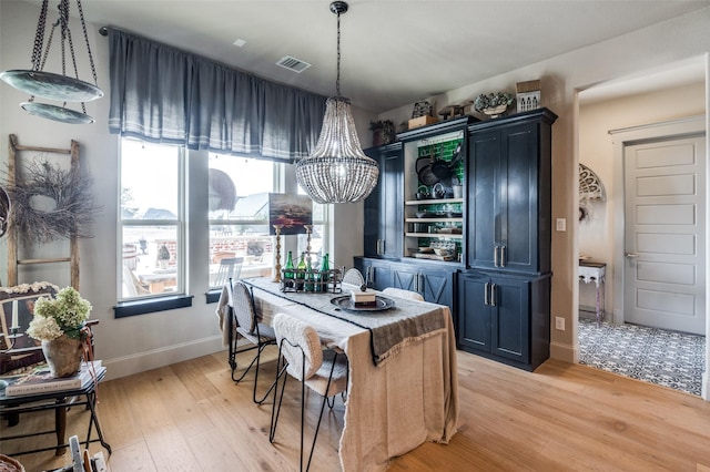 dining area featuring a chandelier, light wood-style flooring, visible vents, and baseboards