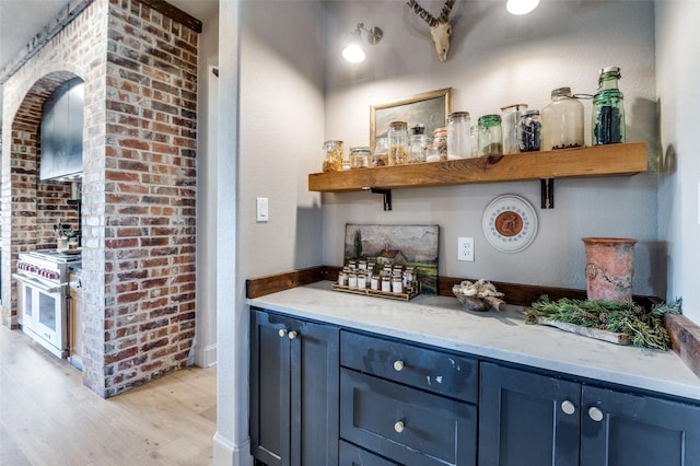 bar with light wood finished floors, double oven range, and brick wall