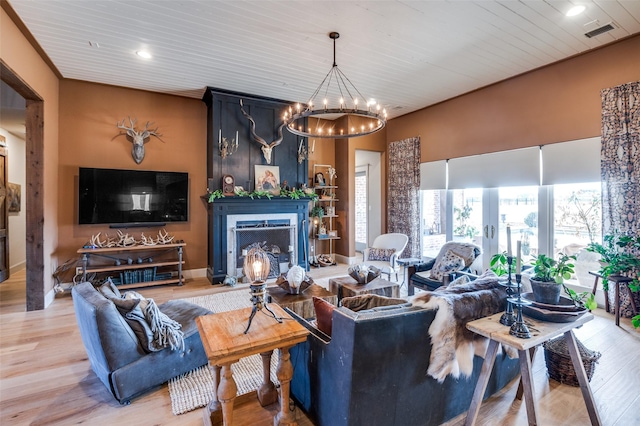 living room with visible vents, a fireplace with raised hearth, wood finished floors, crown molding, and a chandelier