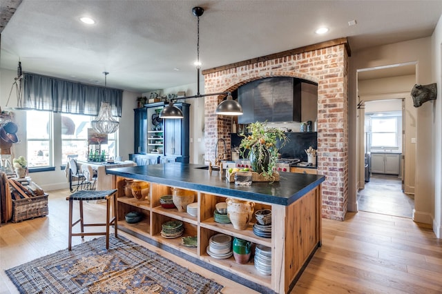 kitchen featuring dark countertops, hanging light fixtures, light wood-style floors, open shelves, and a sink