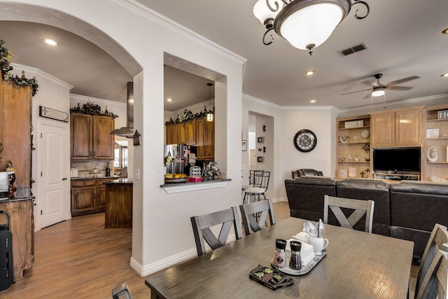 dining room featuring visible vents, arched walkways, ceiling fan, ornamental molding, and wood finished floors