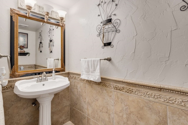 bathroom with a wainscoted wall, a sink, and tile walls