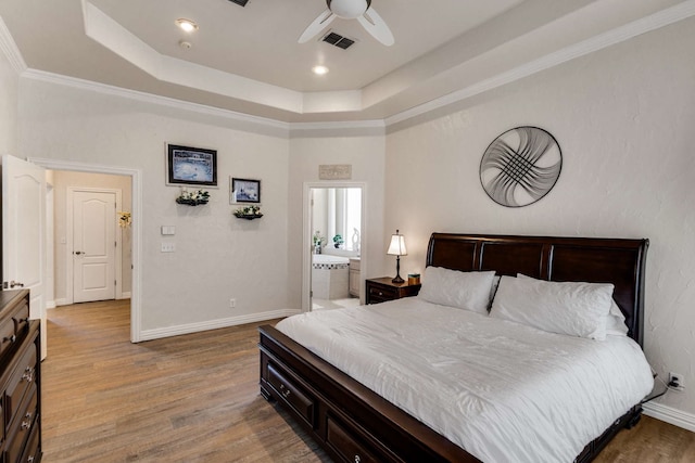 bedroom with baseboards, visible vents, ornamental molding, a tray ceiling, and light wood-style floors