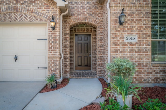 view of exterior entry with an attached garage and brick siding